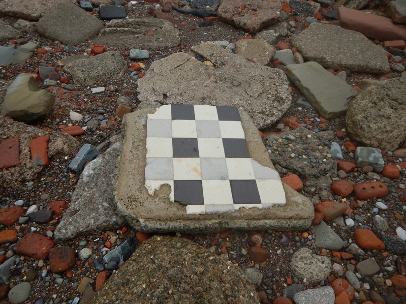 A fragment of concrete floor with black and white tiles intact
